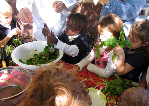 A child helps make the salad before sampling.