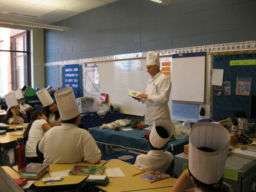 Chief Chef goes over cooking instructions with students at the Chicago Chefs Moves to School Event